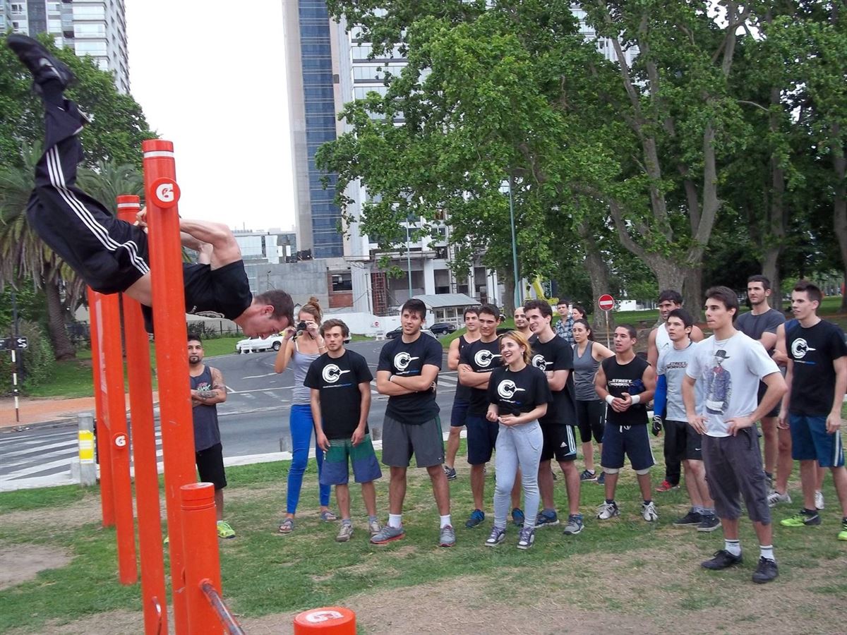 Un compañero hace un ejercicio colgado de los caños de un parque de Palermo mientras más de veinte personas miran; entre ellas, Christian García