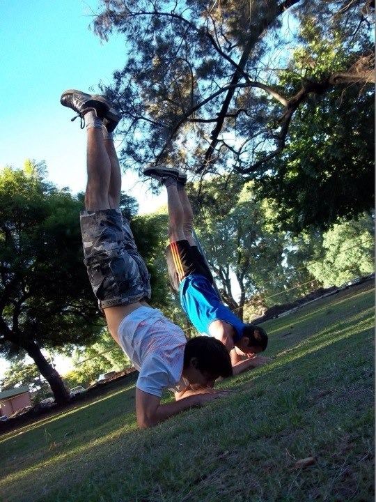 Christian García haciendo una vertical sobre el pasto junto a un compañero